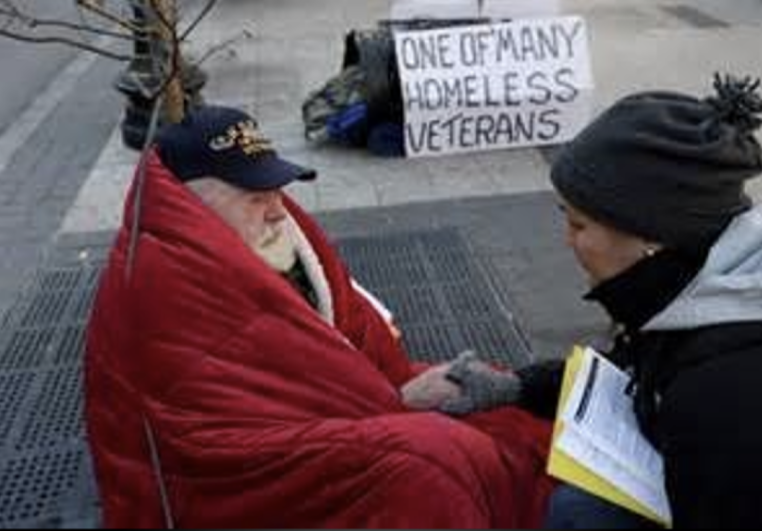 A volunteer kneeling beside a homeless veteran on the street